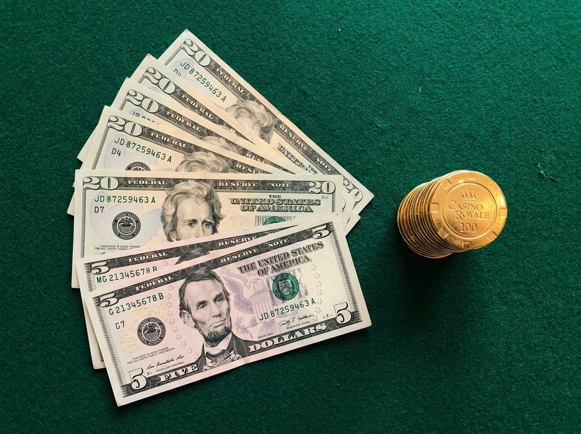 Twenty-five dollar bills fanned out on green casino felt with gold chips
